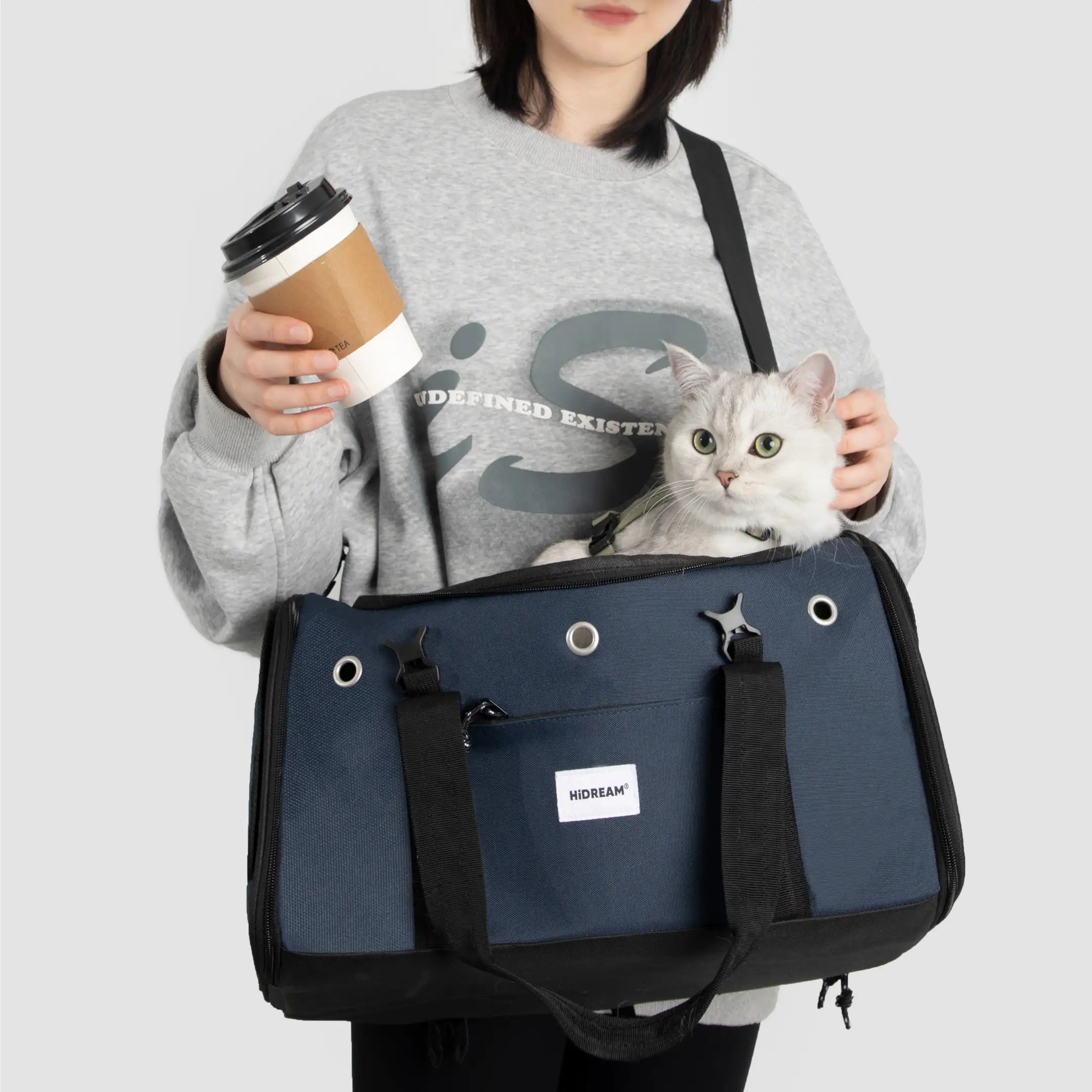 Person holding a coffee cup and a cat in a blue pet carrier against a white background